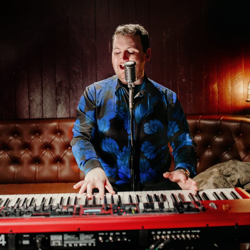 Connor Josef in a blue shirt playing a red piano